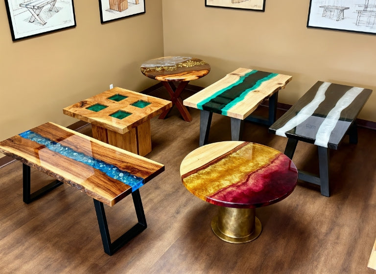 A group of handcrafted live-edge epoxy tables in various styles and colors displayed in a designer’s workshop.