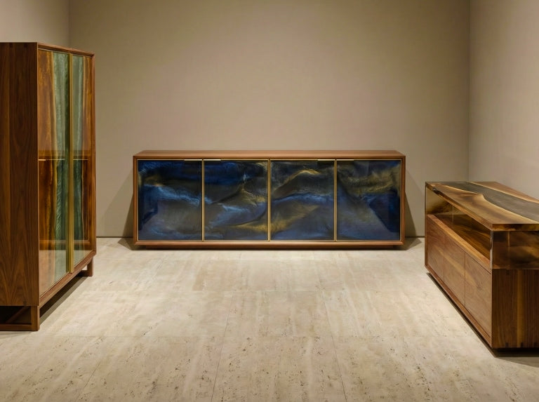 Wide interior view showing multiple wooden storage pieces—a long credenza with blue epoxy panels, a tall glass-front cabinet, and a low console—arranged in a clean, softly lit room with neutral walls and stone flooring.