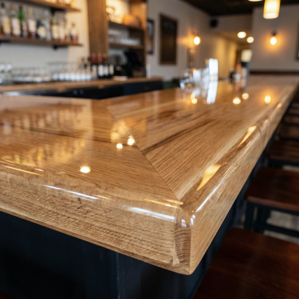 Close-up of a crystal-clear epoxy-coated wooden bar top with rounded edges and rich oak grain in a warmly lit pub.