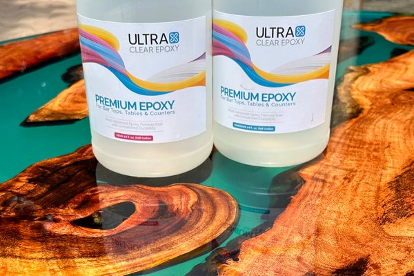 An elaborate epoxy river table with a round shape, made using several pieces of an almost orange-like wood and UltraClear Epoxy. Two bottles of UltraClear Bar & Table Top Epoxy are resting on the surface.
