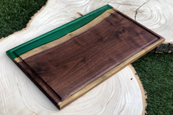An epoxy river charcutire board. It consists of a carved piece of wood and a molded green opaque epoxy river vein.