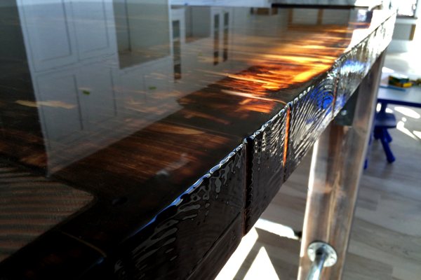 Close-up view of a thick wooden dining table with an UltraClear Bar & Table Top Epoxy finish. It has been expertly applied to a clean, smooth surface.