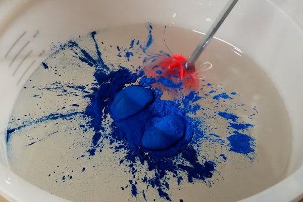A batch of epoxy being mixed with vivid blue powder pigment using a power drill with a mixing bit.