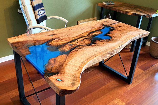 A live-edge wooden epoxy river table, with an epoxy seal coat, a blue-tinted UltraClear Deep Pour Epoxy vein, and an UltraClear Table Top Epoxy coating.