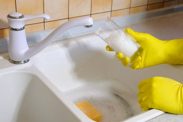 A person washing a resin cup with soap and warm water.