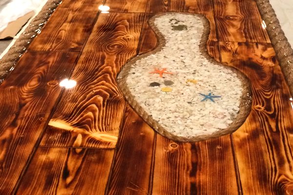 A commercial epoxy bar top with a seabed theme, featuring embedded seashells, starfish, and more. The bar is primarily wood and has been fully sealed with UltraClear Bar & Table Top Epoxy.