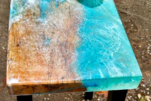 An ocean-themed epoxy end table, consisting of a piece of wood, a thick UltraClear Deep Pour Epoxy layer of turquoise-pigmented epoxy, and a foamy white layer of epoxy to represent convey motion.