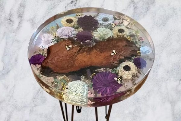 A small round end table with a table top consisting almost entirely of UltraClear Deep Pour Epoxy. Within the epoxy are embedded flowers and small piece of wood.