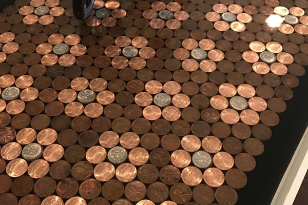 A close-up view of an epoxy penny console table. It consists of a wooden table base with a carefully arrange layer of penies in a floral pattern. The entire top has been sealed with UltraClear Bar & Table Top Epoxy for a perfectly smooth, flat surface.