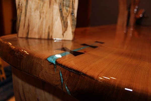 A wooden DIY epoxy bar top with an UltraClear Bar & Table Top Epoxy finish. A small crevice in the wood has been filled with turquoise-pigmented epoxy.