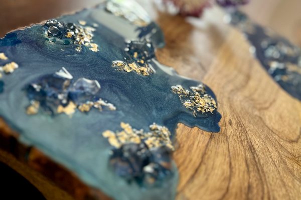A work of resin art consisting of a piece of wood with partial layers of blue-pigmented UltraClear Art & Craft Epoxy, gold flakes, and crushed glass.