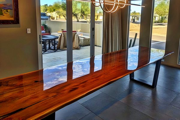 A long wooden epoxy table top in a dining room with many windows.