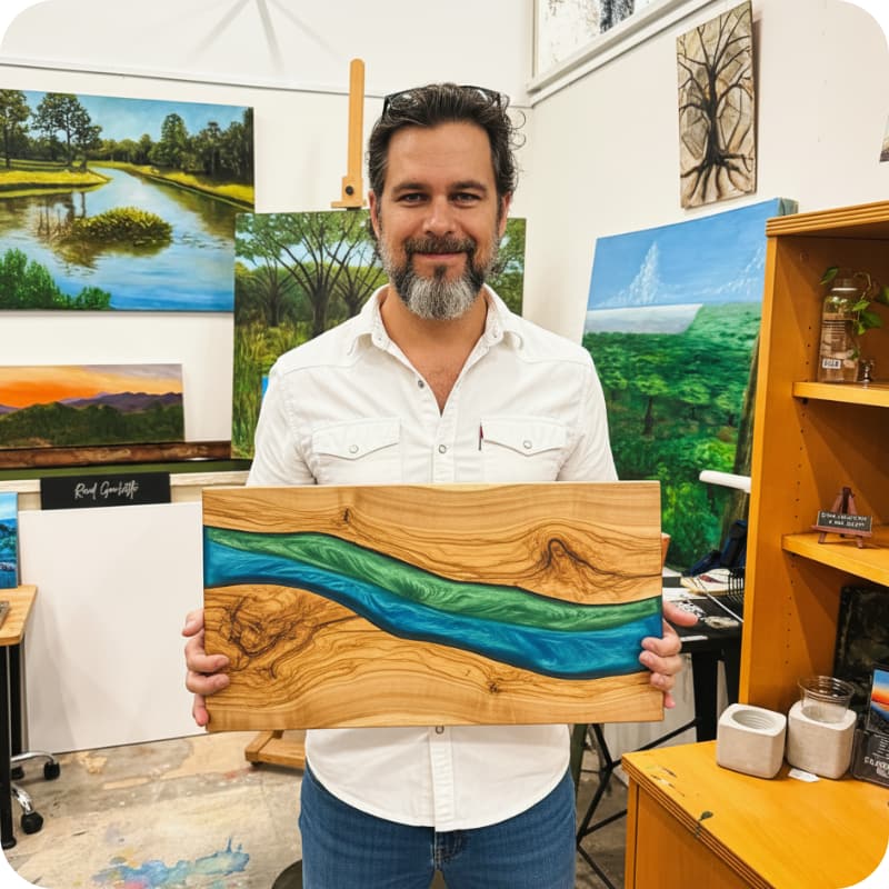 Man holding an epoxy wooden artwork with a colorful design in an art studio filled with paintings.