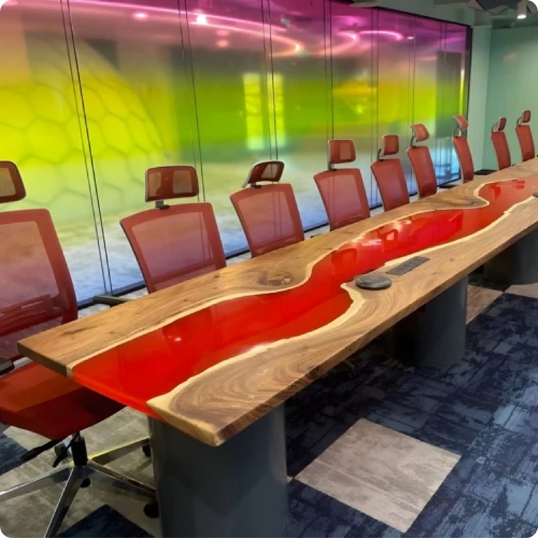 Modern conference room with a long wooden table and red chairs against a colorful wall.