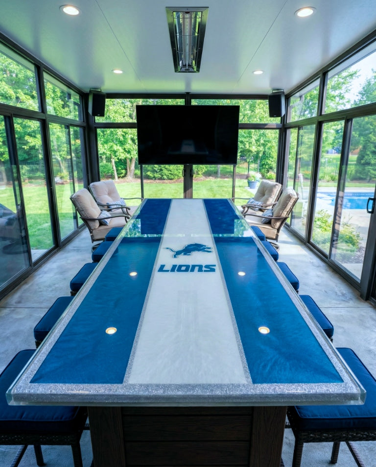 Detroit Lions–themed sunroom bar with a deep-pour epoxy table top in blue and white stripes, silver border, and logo, facing a large TV.