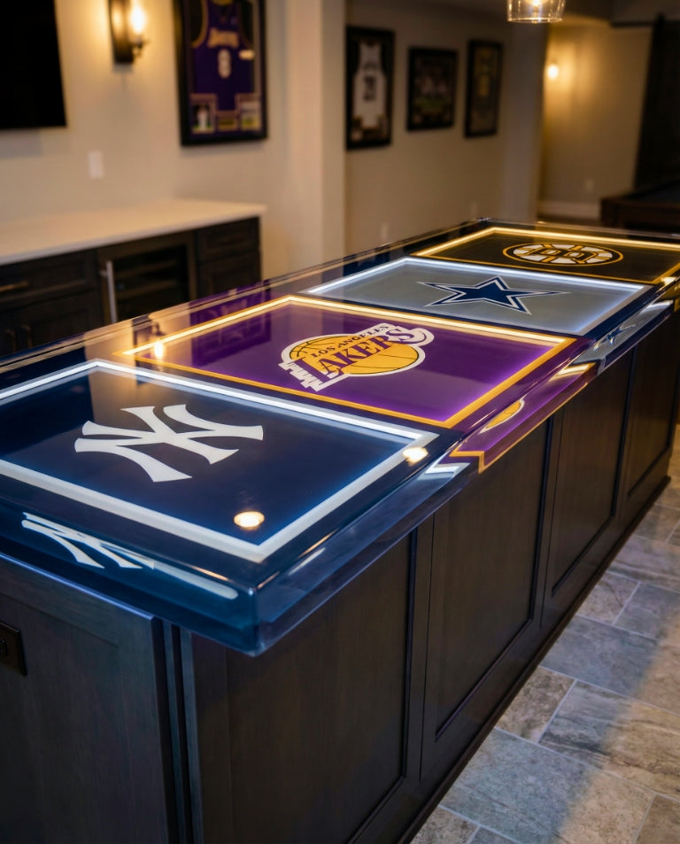 Deep-pour epoxy bar top with embedded Yankees, Lakers, Cowboys, and Bruins logos, each framed by subtle under-epoxy lighting in a refined home bar.