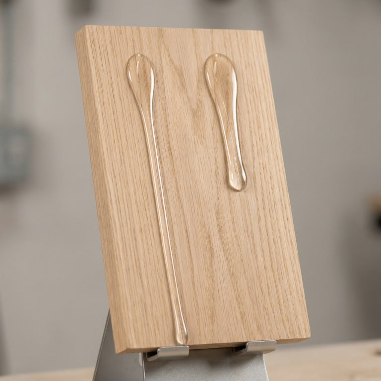 Clear epoxy drips on an inclined wooden board, showing one long thin flow and one shorter thicker flow to illustrate differences in epoxy viscosity.