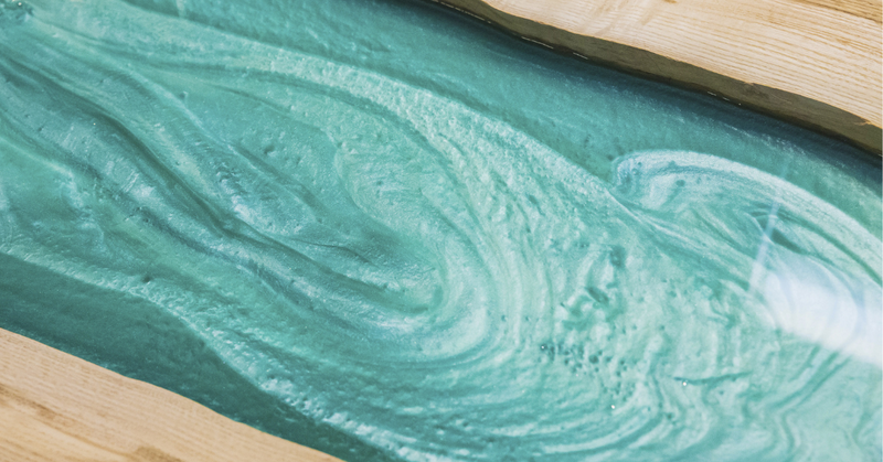 A close-up view of an epoxy river table vein, tinted teal