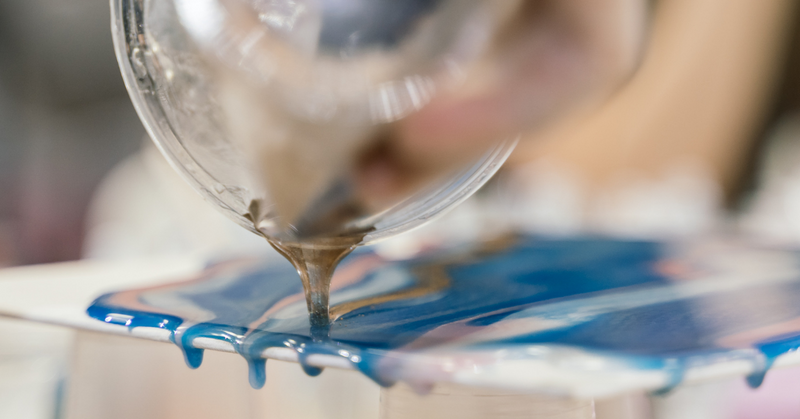 Epoxy resin being poured onto a thin, flat piece of wood