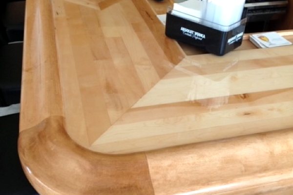 A close-up view of one corner of a U-shaped wooden epoxy bar top. A perfectly smooth UltraClear Bar & Table Top Epoxy finish can be seen over the wooden substrate.