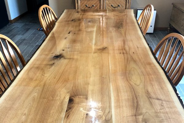 A large live-edge wooden dining table with an UltraClear Bar & Table Top Epoxy.