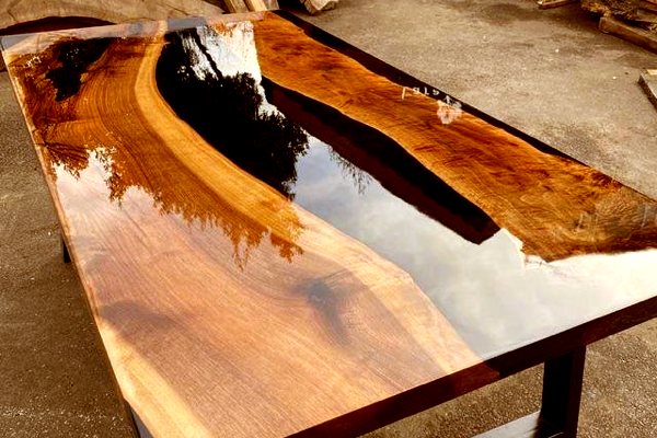 A beautiful epoxy river table with a deep black river vein made using UltraClear Deep Pour Epoxy. It's sitting outside, and a reflection of the sky can be see in its glass-like finish.