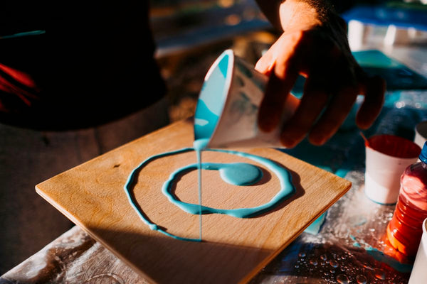 Blue-pigmented epoxy resin being poured in a spiral pattern onto a square of wood