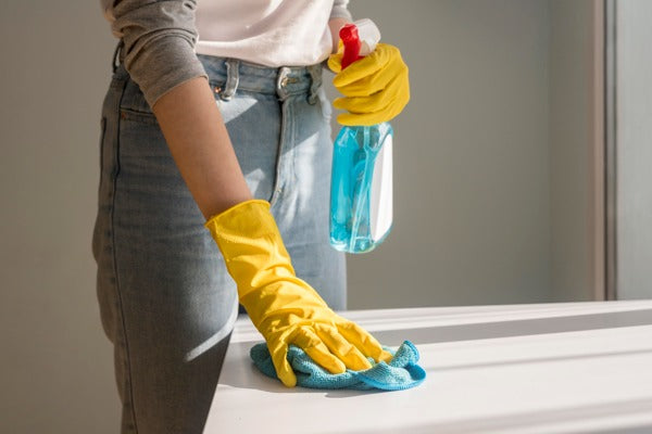 A gloved hand wiping down an epoxy surface with glass cleaner and a microfiber cloth.