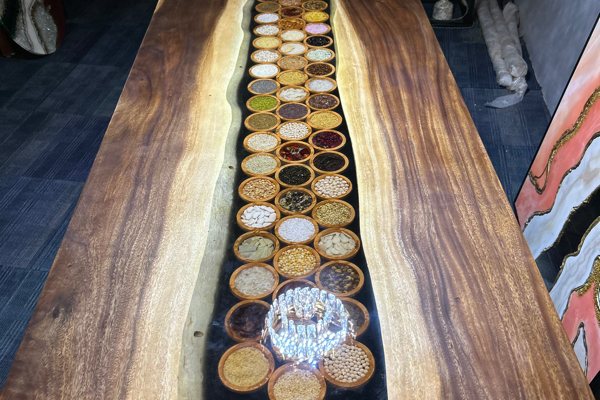 An elaborate epoxy river table with a wide transparent river vein of UltraClear Deep Pour Epoxy containing various small dishes filled with dried plant foods.