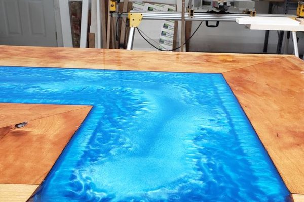 A wooden epoxy countertop with a wide river vein tinted with bright blue epoxy pigments.