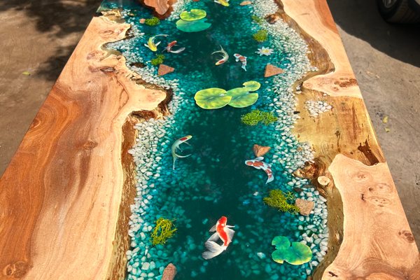 An epoxy coffee table with a very wide river vein and layered embedments used to convey a 3D depiction of a river bed. There are pebbles, fish, and aquatic flora embedments within the epoxy vein.