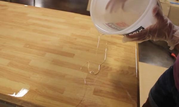 A person carefully pouring epoxy resin onto a wooden countertop