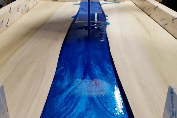 An blue-pigmented epoxy river vein being poured in between two pieces of wood which have been contained by a temporary dam.