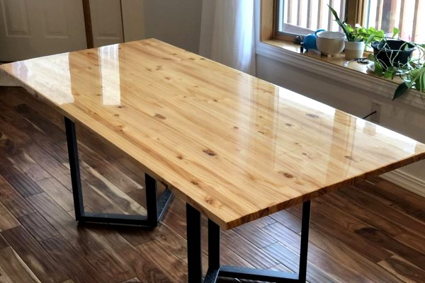 A simple wooden dining table consisting of a flat rectangular piece of wood, metal table legs, and a transparent coating of UltraClear Bar & Table Top Epoxy. It is well maintained.