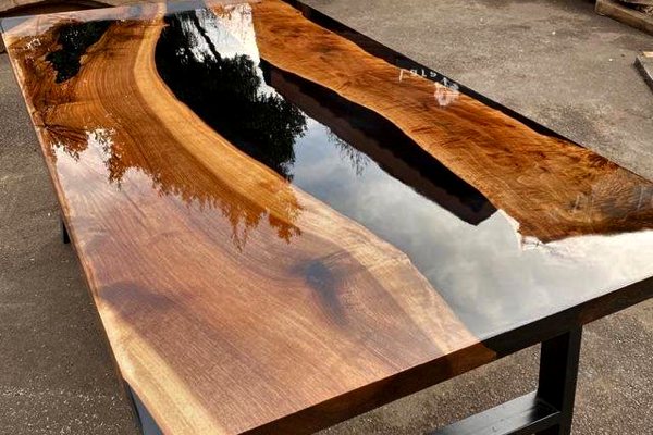 A rectangular epoxy river table with a pure-black opaque UltraClear Deep Pour Epoxy river vein and two large slabs of wood. It's been topcoated with UltraClear Bar & Table Top Epoxy.