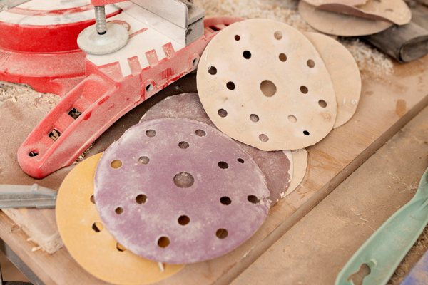 A photo of a power sander and several dirty sanding discs meant for it.