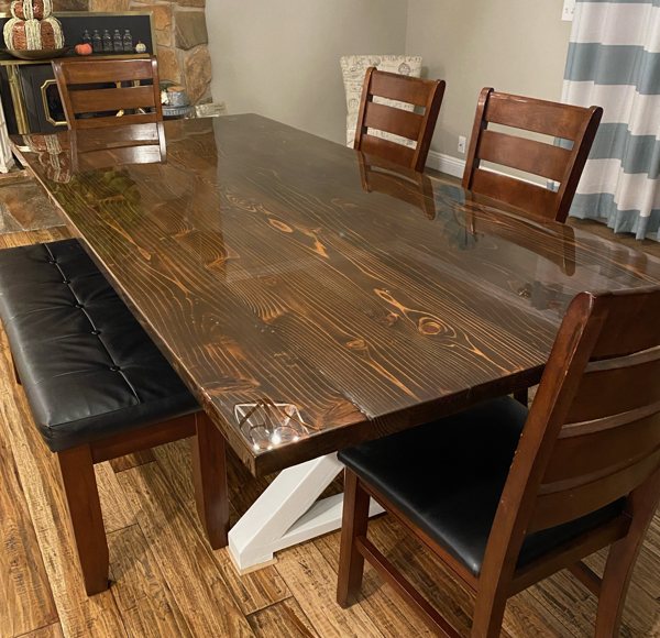 A wooden epoxy resin table top with several wooden chairs surrounding it.