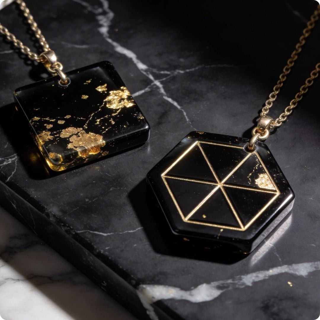 Two black pendants with gold designs on a dark marble surface